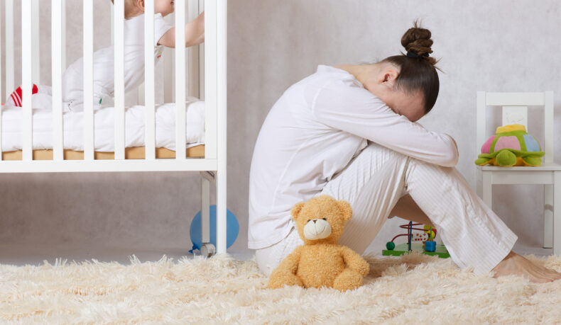 O femeie care stă deprimată lângă pătuțul copilului