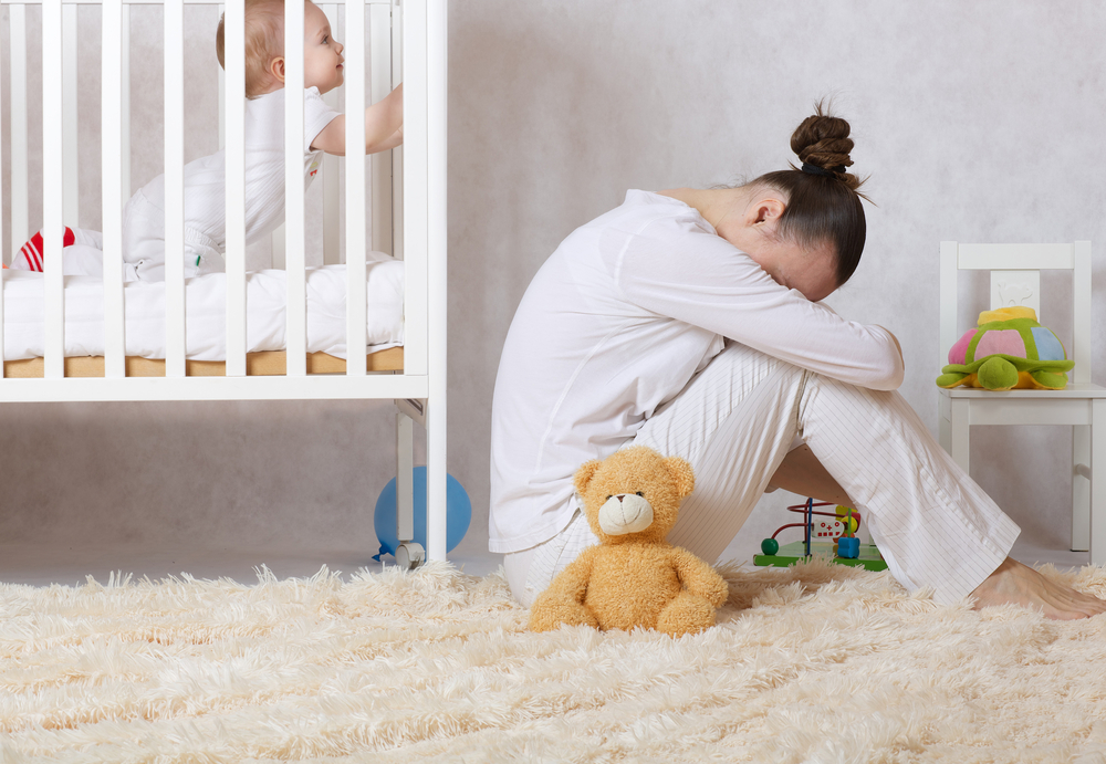 O femeie care stă deprimată lângă pătuțul copilului
