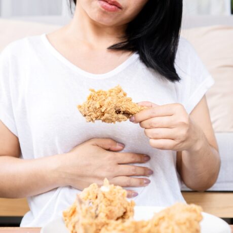Femeie care mănâncă pui prăjit și are dureri de stomac date de gastrită