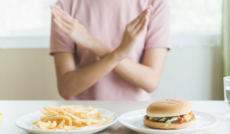 Femeie care refuză cartofi prăjiși și hamburger, aliemnte care trebuie excluse din dieta în artrită