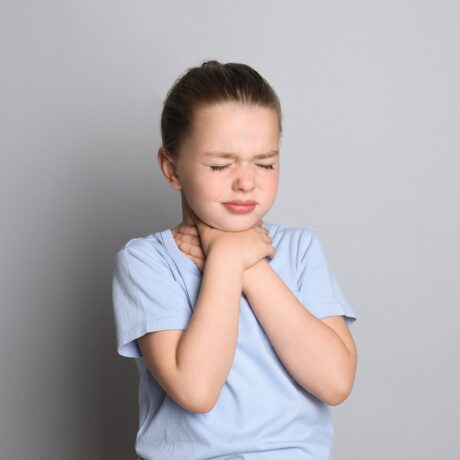 Fetiță care ține mâinile la gât și are dureri cauzate de laringita acută