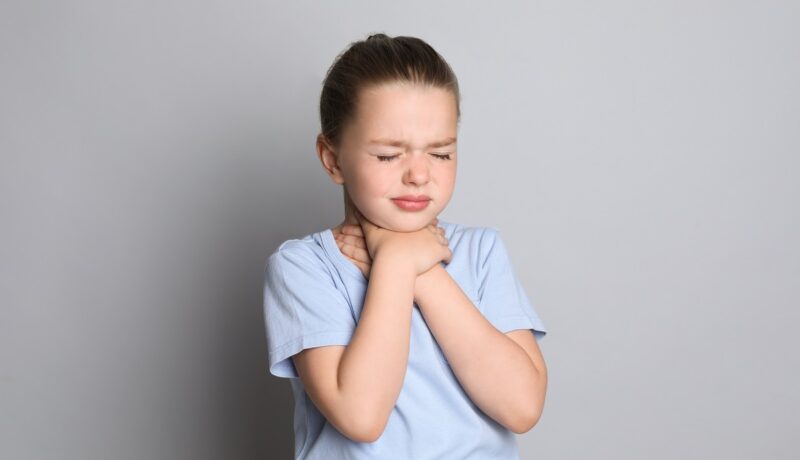 Fetiță care ține mâinile la gât și are dureri cauzate de laringita acută