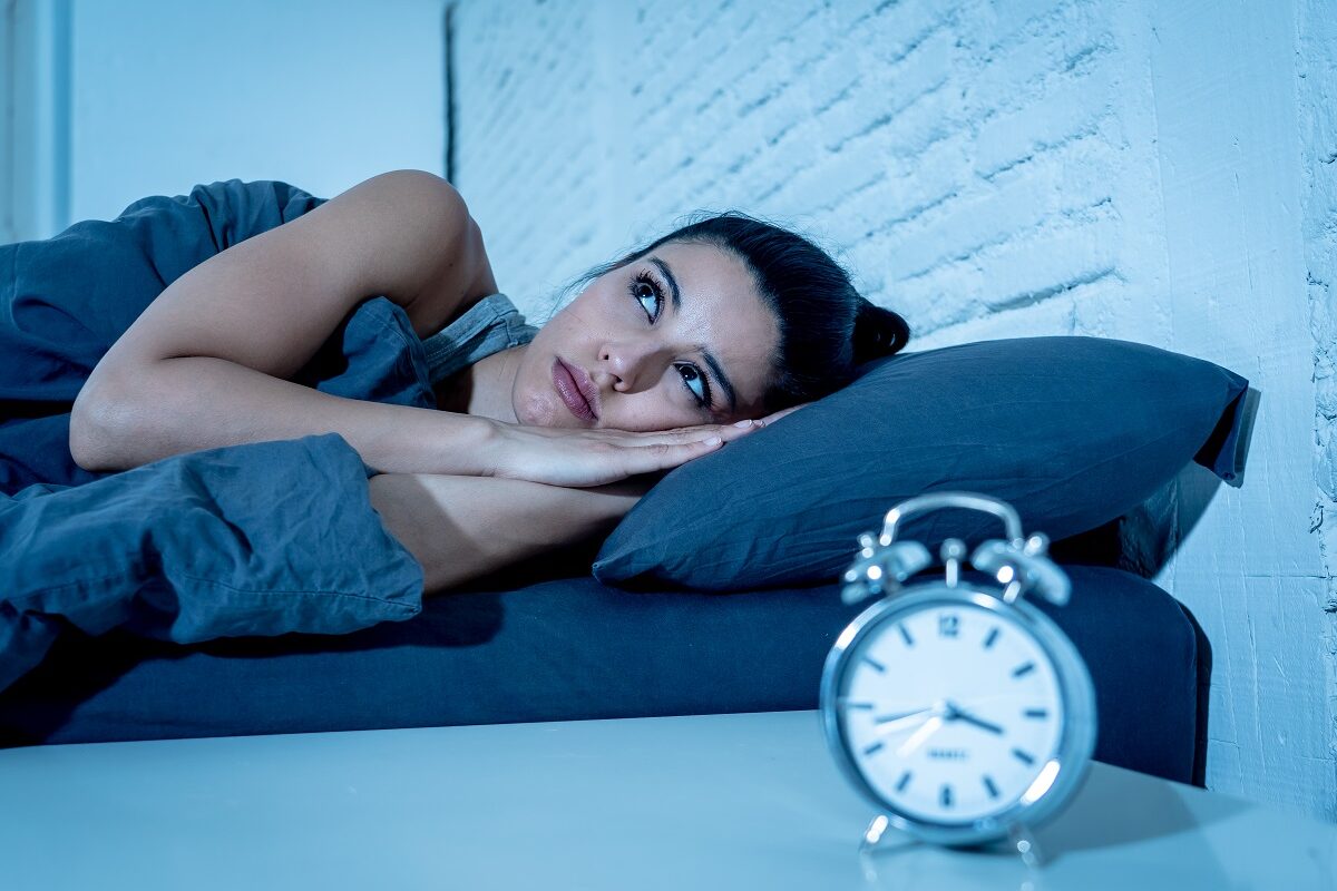 Femeie care stă în pat și nu poate să doarmă noaptea din cauza unor tulburări de somn