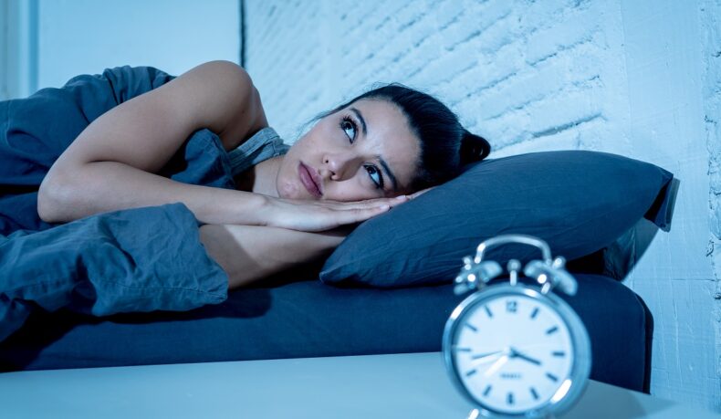 Femeie care stă în pat și nu poate să doarmă noaptea din cauza unor tulburări de somn