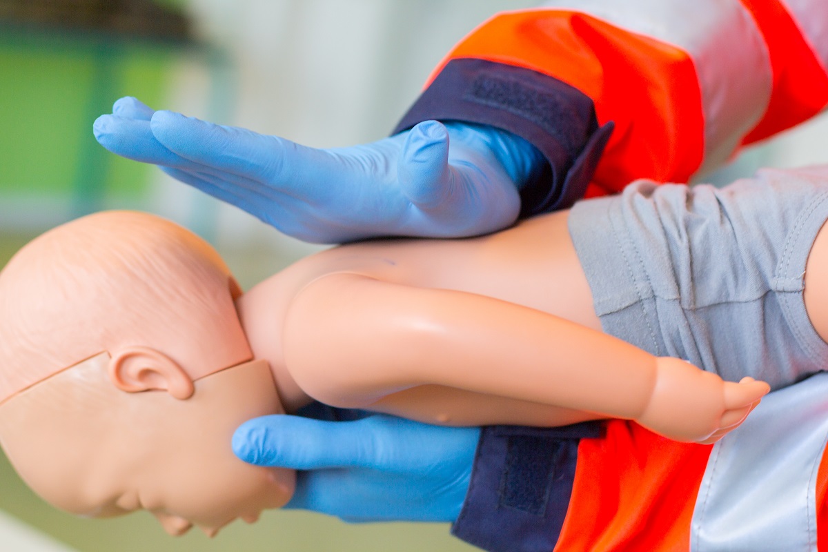 Paramedic care acordă unui bebeluș de jucărie primul ajutor în caz de înec cu lapte sau mâncare