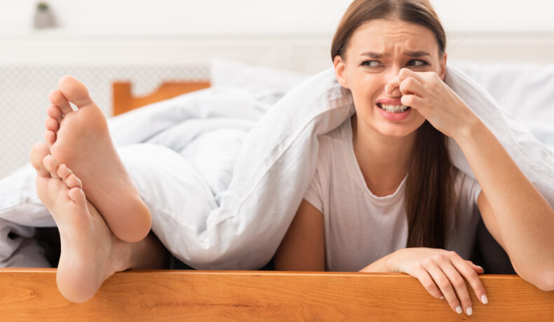 O femeie care se ține de nas din cauza mirosului urât al picioarelor partenerului