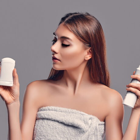 O fată, acoperită de un prosop, care ține în mână deodorante de tipuri diferite
