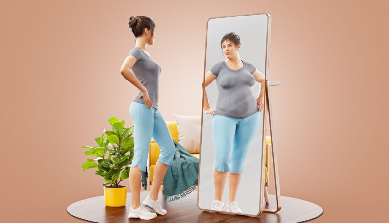 Femeie care se privește în oglindă și se vede mai grasă decât în realitate, simptom care definește bulimia