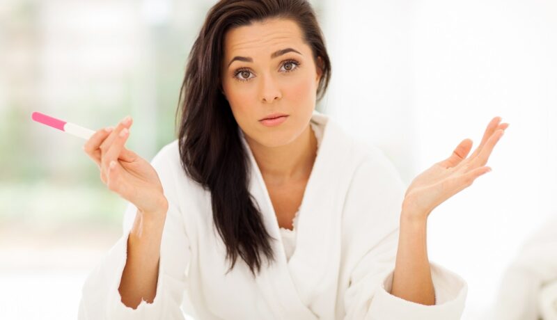 Femeie cu teste de sarcină în mână care întreabă dacă poți face test de sarcină la menstruație
