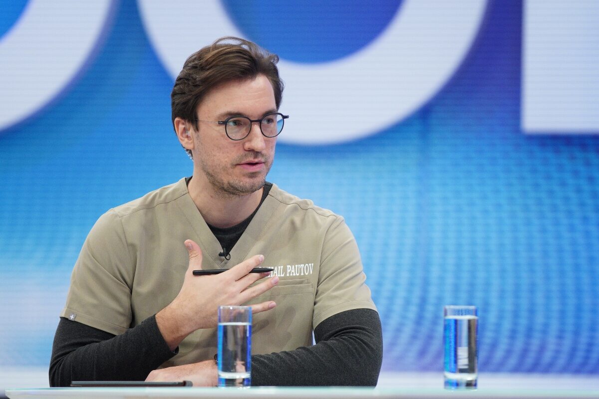 Doctorul Mihail Pautov, în costum de medic, fotografiat în timp ce ține un pix în mână și explică ceva