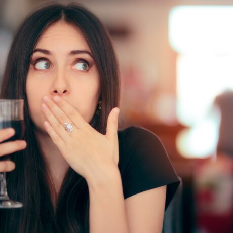 Femeie cu mâna la gură care sughiță și ține în mână un pahar cu suc de culoare închisă
