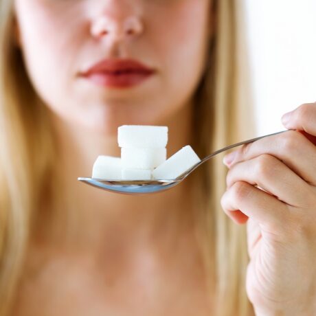 femeie care ține cuburi de zahăr într-o lingură, zahărul de masă fiind unul dintre zaharurile adăugate periculoase pentru inimă