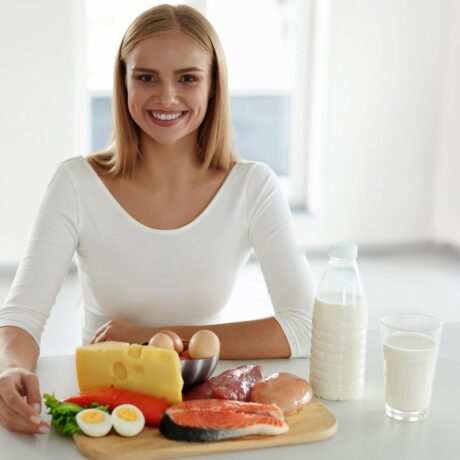 Femeie cu alimente bogate în proteine pe masă: carne, lactate și ouă