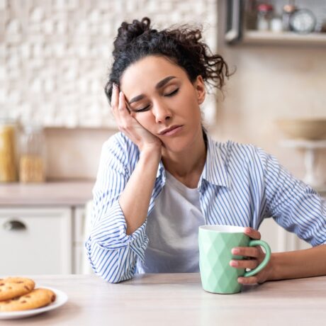 Femeie obosită care doarme cu cana de cafea în mână. Oboseala cronică piate semnala lipsa de fier