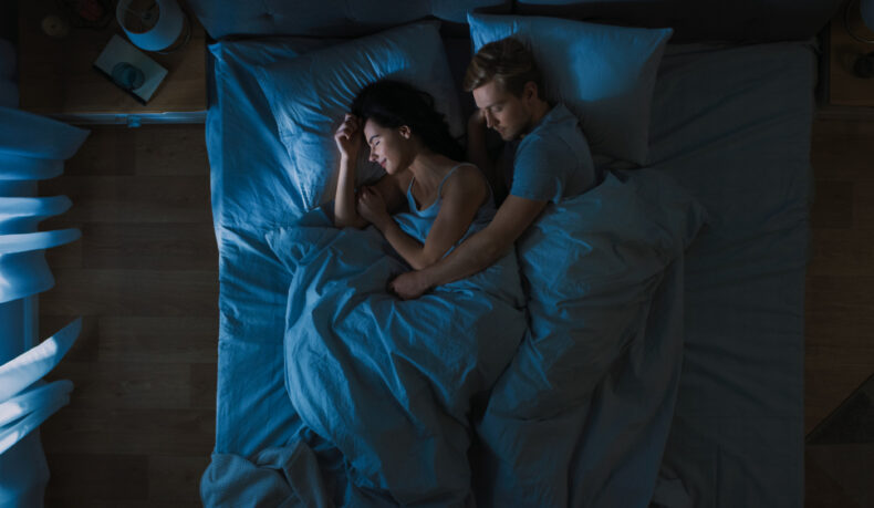 O femeie și un bărbat care dorm într-un pat matrimonial