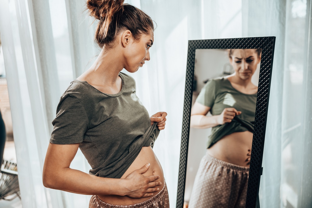 Femeie cu balonare excesivă care își privește abdomenul în oglindă