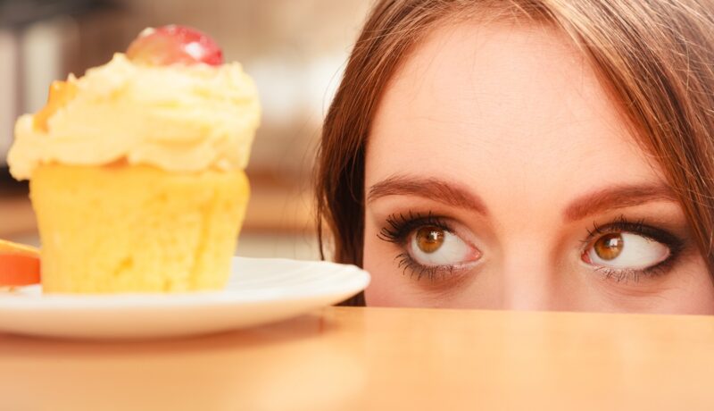 Femeie care privește o prăjitură, sugestiv pentru pofta de dulce