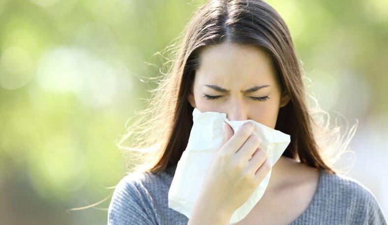 Femeie cu alergie care își suflă nasul, sugestiv pentru alergiile respiratorii