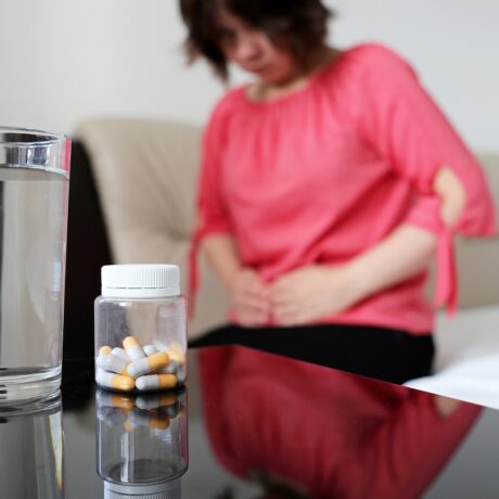 Femeie cu durere de burtă și laxative pentru constipație în prim plan, împreună cu un pahar de apă