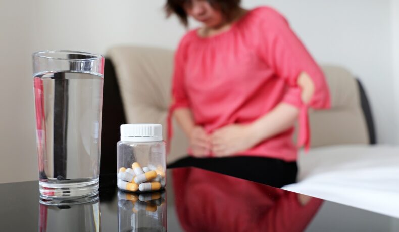 Femeie cu durere de burtă și laxative pentru constipație în prim plan, împreună cu un pahar de apă