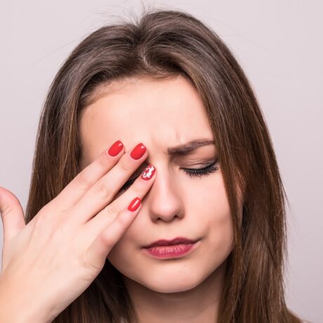 Femeie cu mâna pe ochi, care suferă de durere oculară