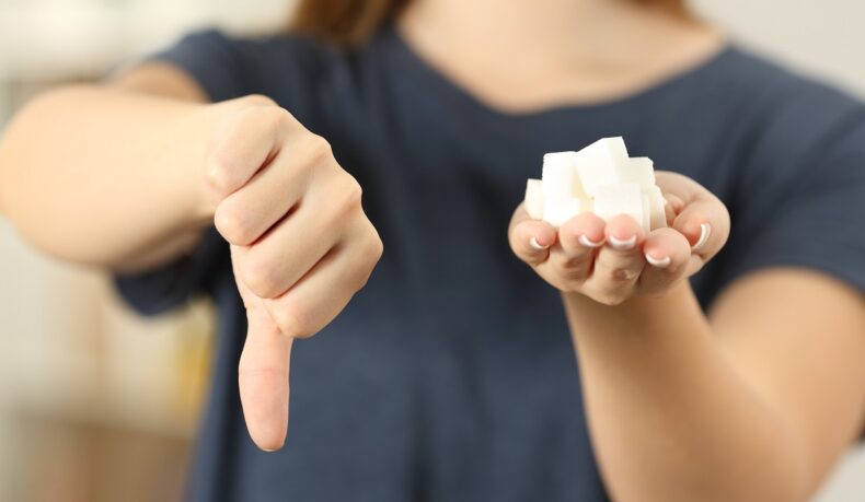 Femeie cu mai multe cuburi de zahăr alb în mână care arată cu degetul un semn de dezaprobare pentru zahărul în exces