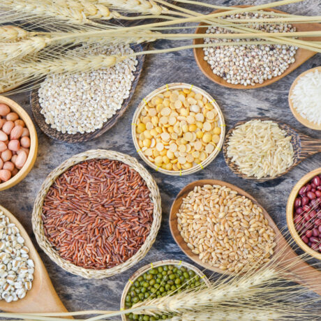 Diverse tipuri de cereale naturale și semințe așezate în boluri și linguri de lemn, pe un fundal decorat cu spice de grâu