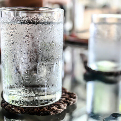 Un pahar cu apă foarte rece, pus pe o masă, în fața unui fundal neclar