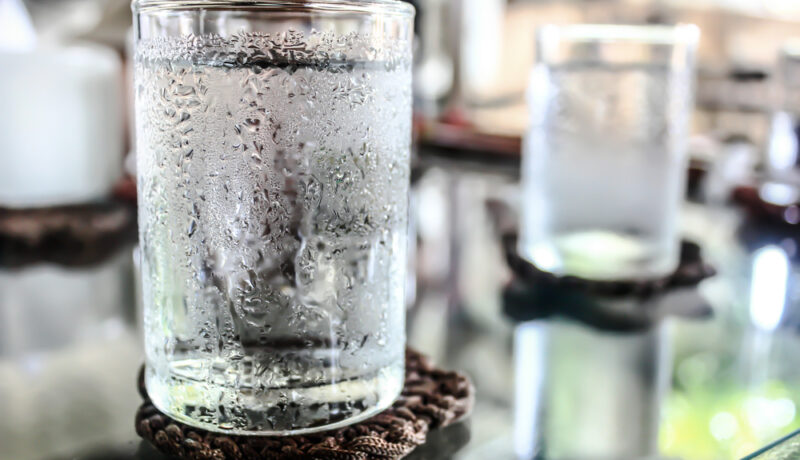 Un pahar cu apă foarte rece, pus pe o masă, în fața unui fundal neclar