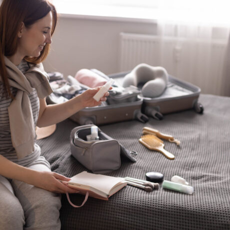 O femeie scrie o listă cu produsele cosmetice și obiectele necesare, stând pe pat