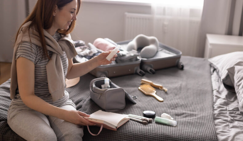 O femeie scrie o listă cu produsele cosmetice și obiectele necesare, stând pe pat