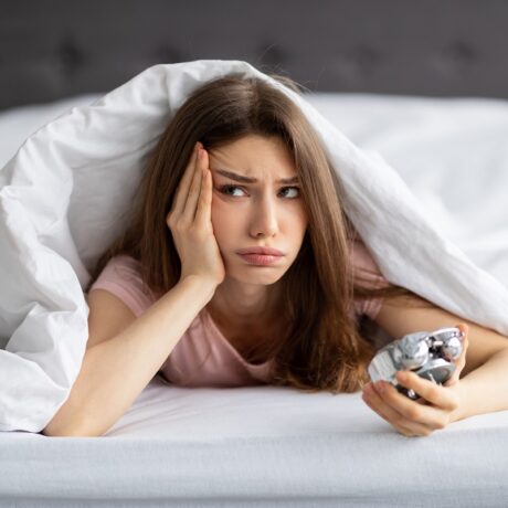 Fata care stă în pat, se uită la ceas și nu poate să adoarmă, în căutare de soluții pentru cum să adormi mai repede
