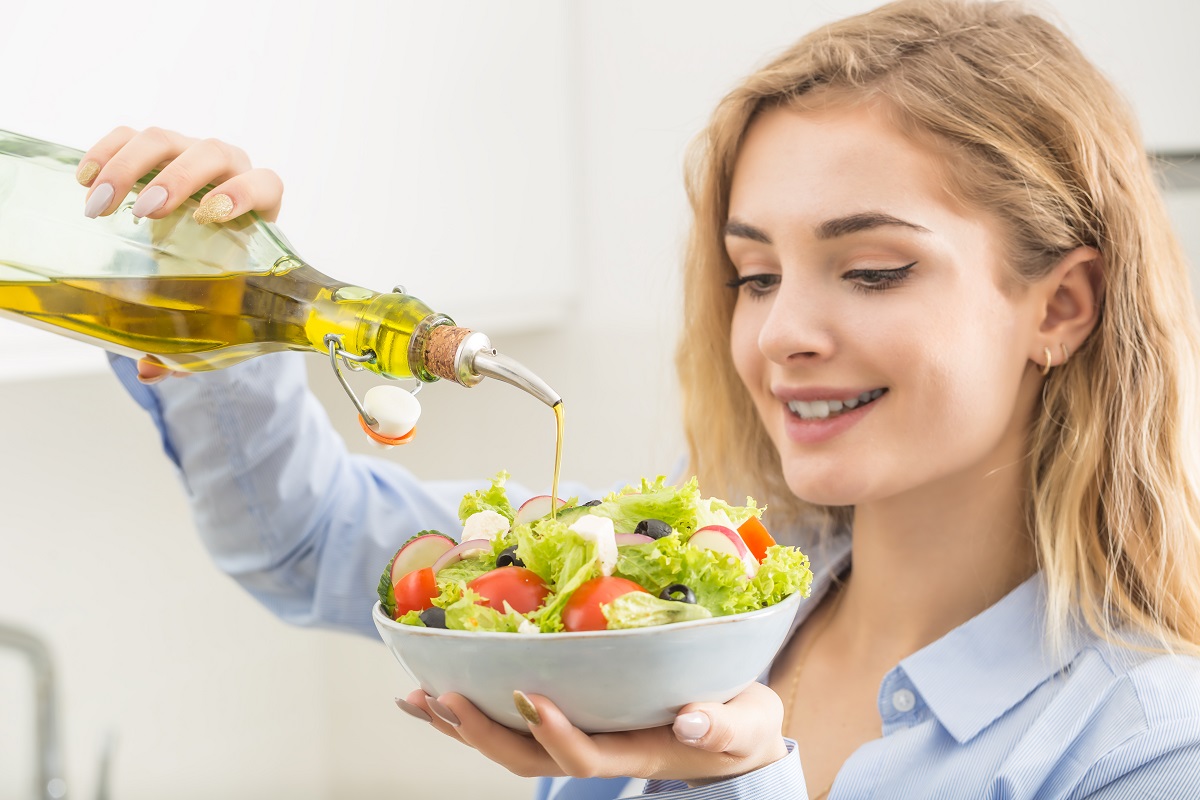 Femeie care prepară o salată cu ulei de măsline, recomandată la începutul mesei, conform unei reguli de alimentație