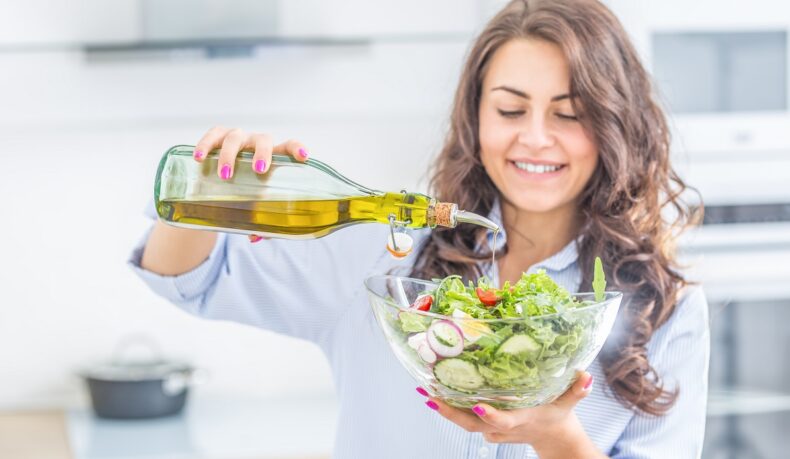 Femeie care toarnă ulei de măslne extravirgin într-o salată
