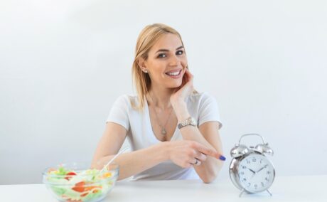 Femeie cu o salată și cu un ceas pe masă, sugestiv pentru postul intermitent