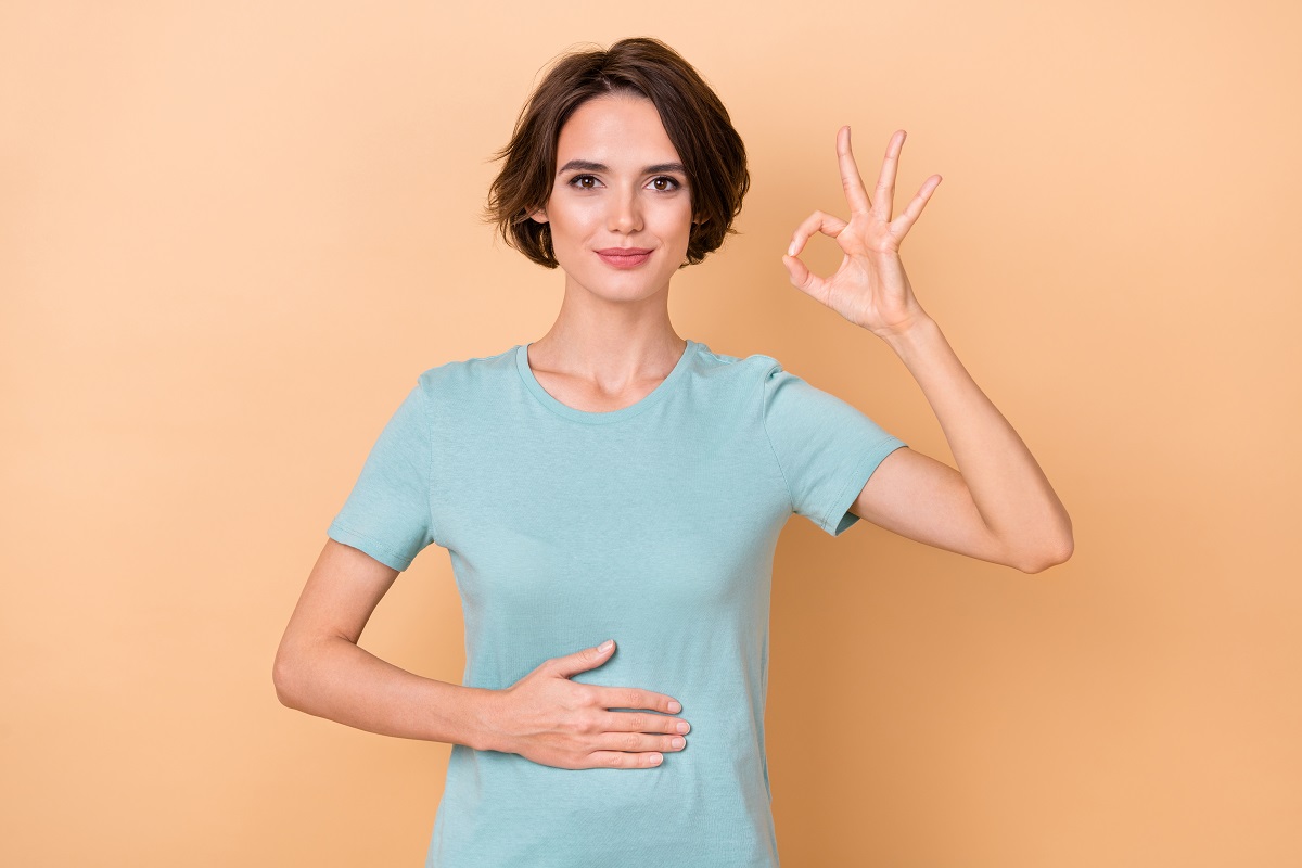 Femeie cu mâna pe burtă care arată semnul OK, sugestiv pentru digestie ușoară și corectă