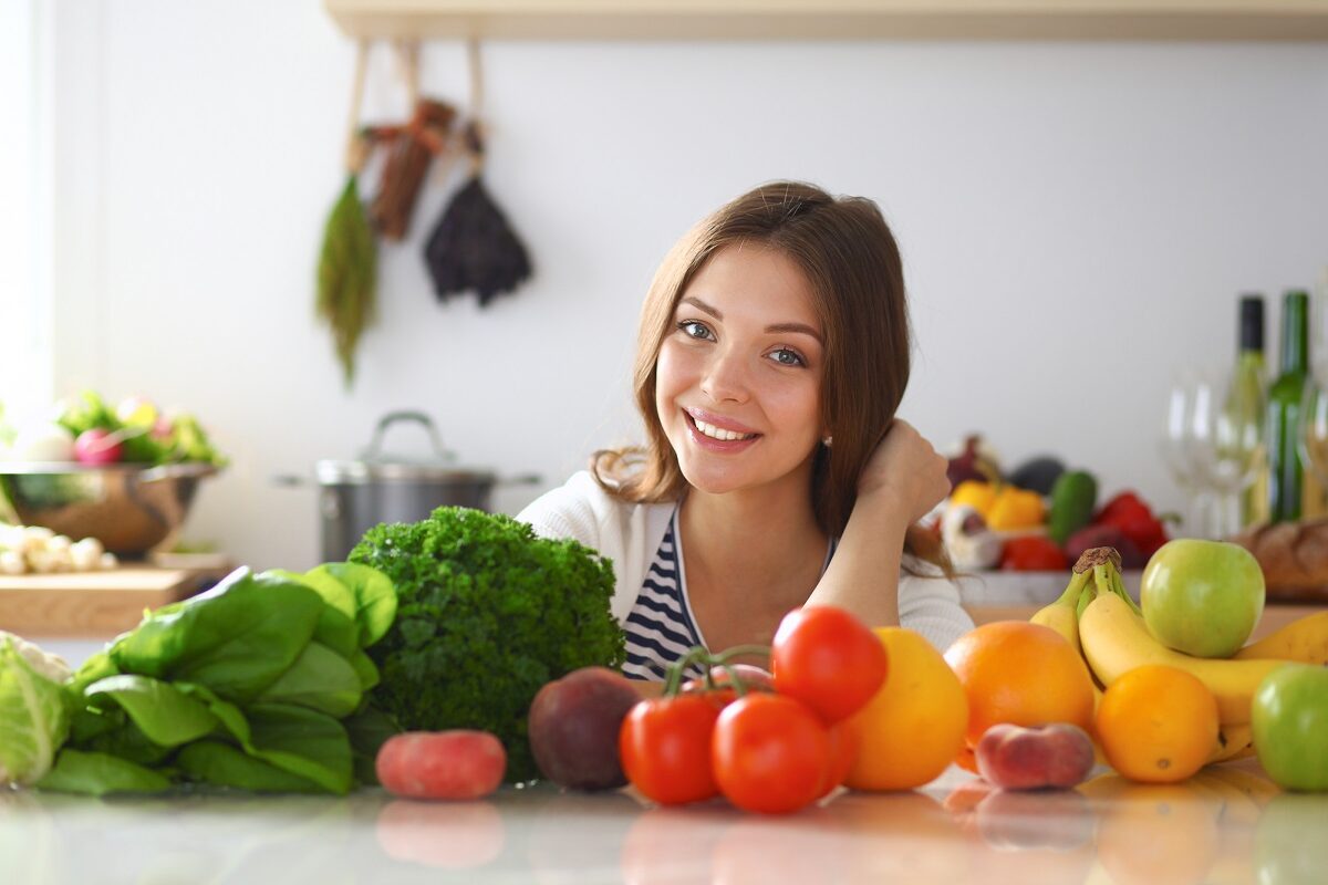 Femeie cu multe legume și fructe pe masă, surse de fibre alimentare care pot să provoace gaze intestinale