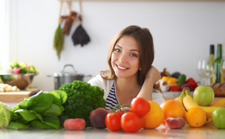 Femeie cu multe legume și fructe pe masă, surse de fibre alimentare care pot să provoace gaze intestinale