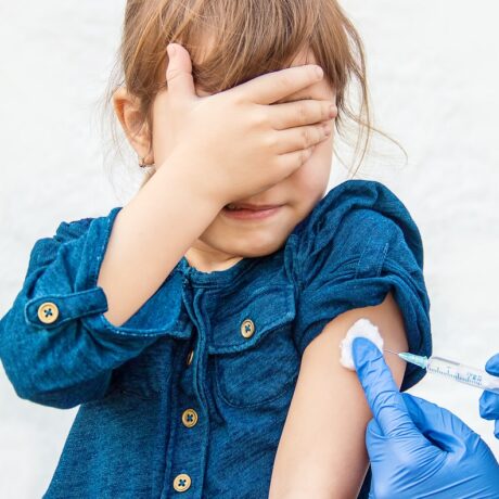 Fetiță care primește un vaccin în braț și își acoperă ochii cu mâna, sugestiv pentru vaccinul antivaricelă la copii