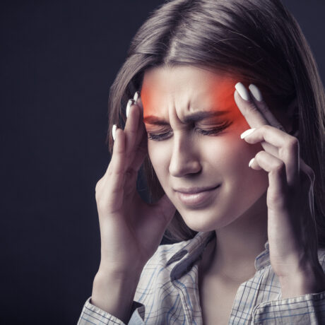 O femeie tânără își ține mâinile la tâmple din cauza unei dureri de cap