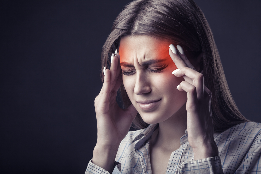 O femeie tânără își ține mâinile la tâmple din cauza unei dureri de cap