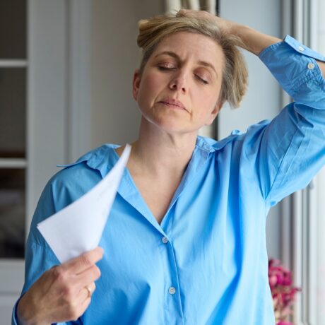 Femeie cu bufeuri la menopauză care se răcorește cu un ventilator