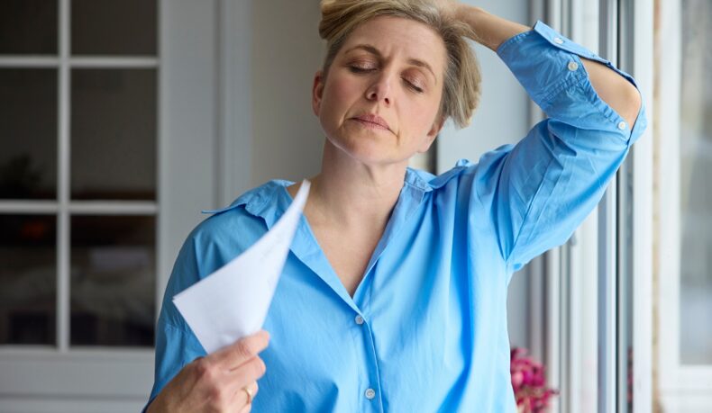 Femeie cu bufeuri la menopauză care se răcorește cu un ventilator