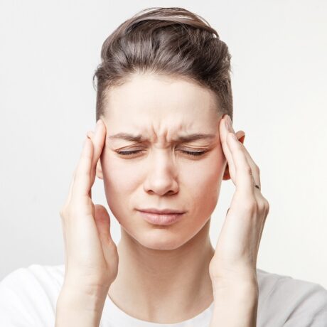 Femeie cu dureri de cap, cu mâinile la tâmple, sugestiv pentru harta durerilor de cap