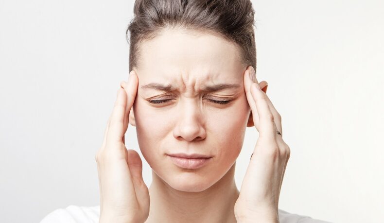 Femeie cu dureri de cap, cu mâinile la tâmple, sugestiv pentru harta durerilor de cap