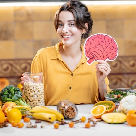 Femeie cu multe legume și fructe ce conțin antioxidanți care previn boala Alzheimer și cu un creier desenat pe care îl ține în mână