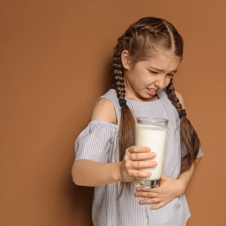 Fetiță cu pahar de lapte în mână și durere de burtă, sgestiv pentru alergiile alimentare la copii
