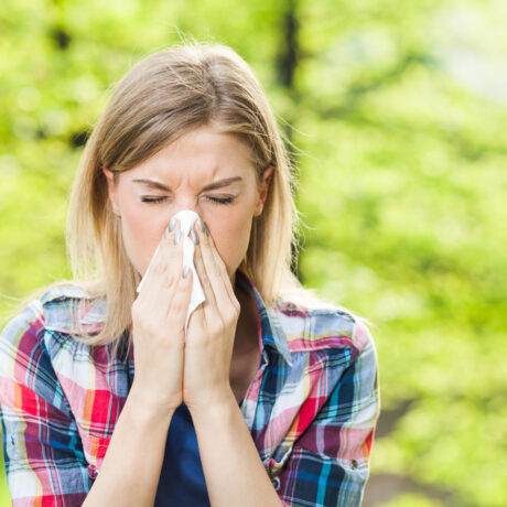 O femeie tânără își ține nasul într-o batistă, din cauza unei alergii