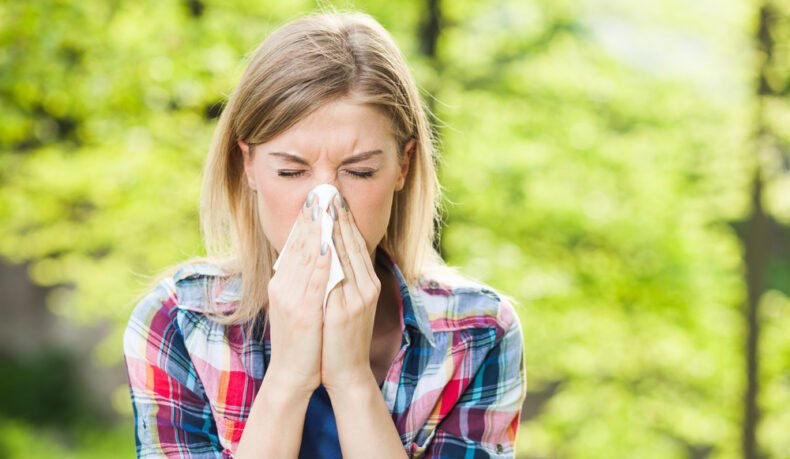 O femeie tânără își ține nasul într-o batistă, din cauza unei alergii