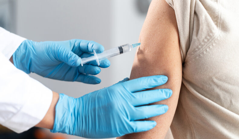 Un femeie cu mănuși de protecție, injectează o doză de vaccin unui pacient